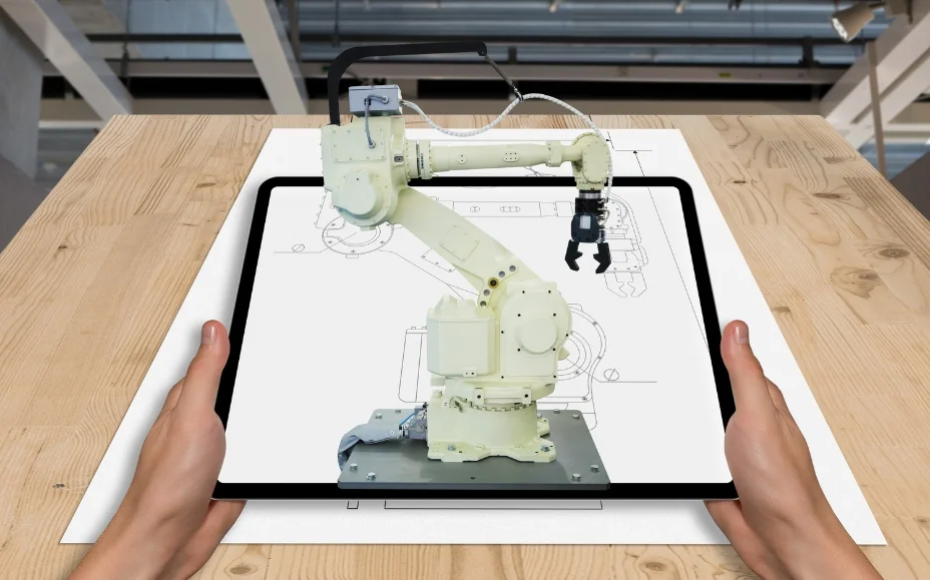 Tablet showing a robotic arm model over a blueprint, held by two hands on a wooden table in a workshop