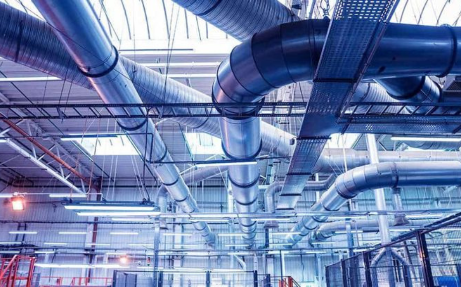 Industrial facility ceiling with large interconnected metal ducts and pipes forming a complex HVAC network.