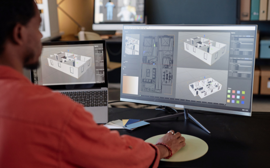 Designer working on 3D architectural models on a large monitor and a laptop at a desk.