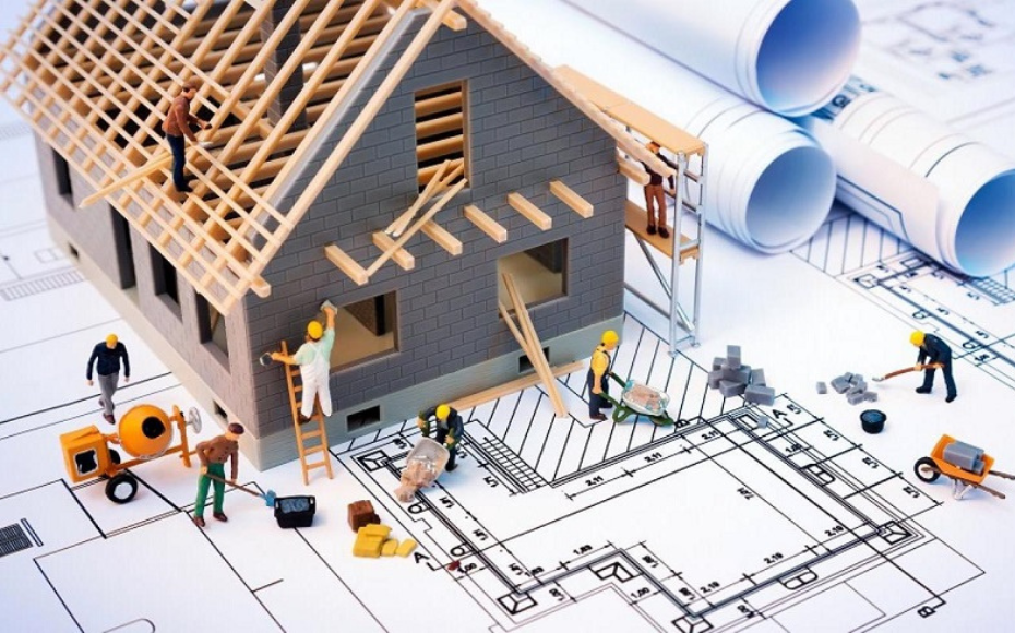 Miniature construction crew building a model house on top of architectural blueprints.