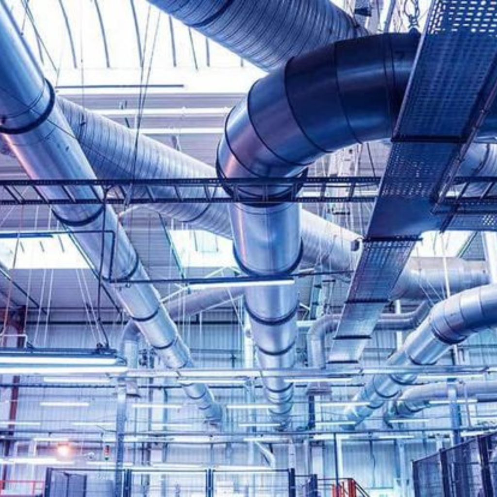 Ceiling view of a large industrial facility with numerous metal ducts and pipes running overhead.