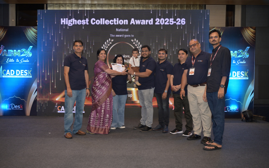 Group of colleagues on a stage accepting the Highest Collection Award 2025-26; a woman in a purple sari hands a certificate and trophy to a man holding a small child, flanked by teammates.