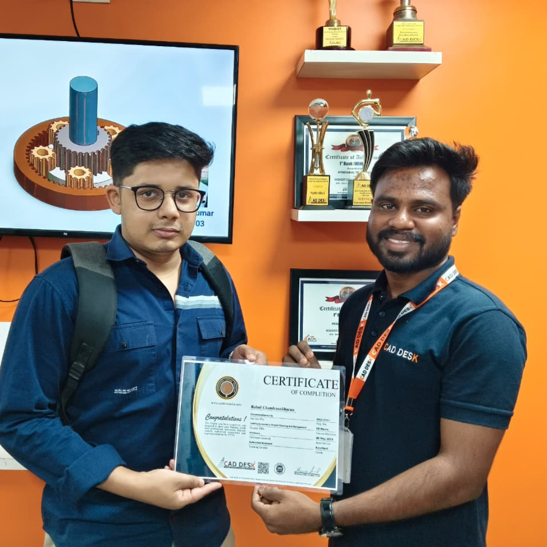 Two men stand before an orange wall as one hands a certificate to the other, trophies on a shelf behind them.