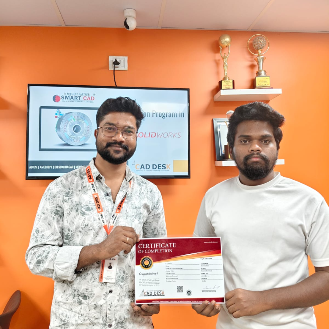 Two men pose indoors as one hands a certificate of completion to the other, with an orange wall, TV screen, and trophies behind them.
