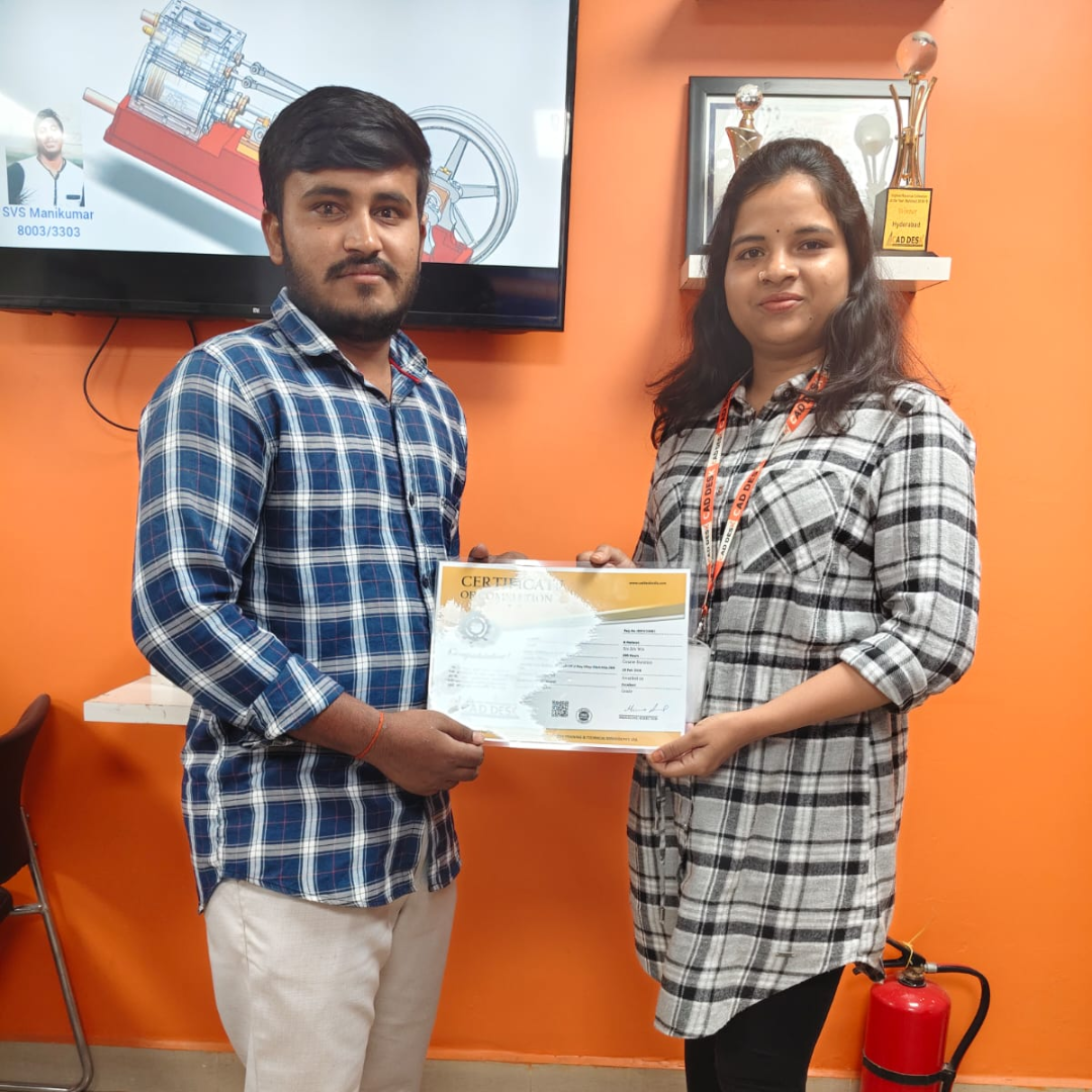 Two coworkers pose as a certificate is handed over in front of an orange wall during a recognition moment.