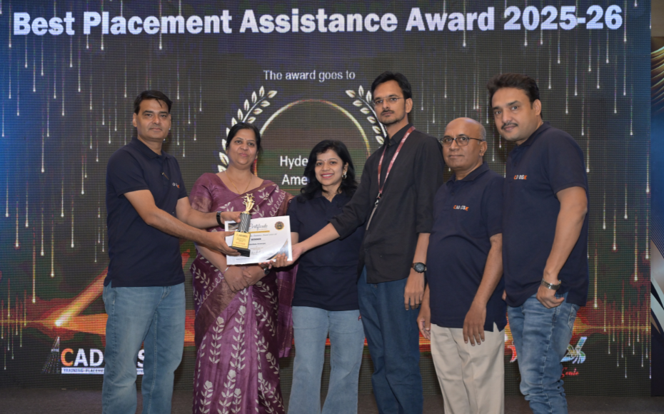 Six people on stage at an awards ceremony; a woman in a purple saree hands a trophy and certificate to a man while others pose nearby