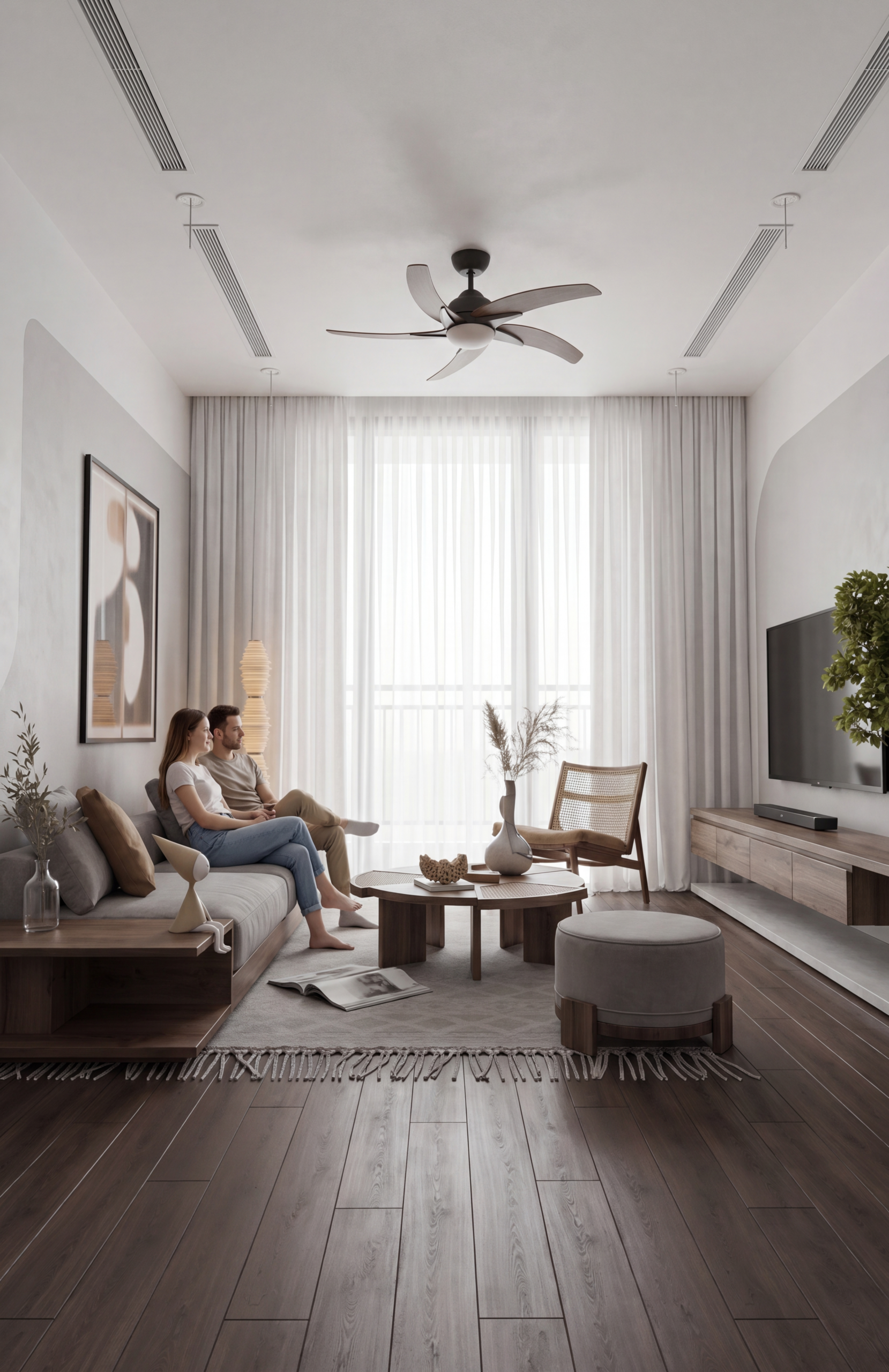 Modern living room with two people sitting on a gray sofa, ceiling fan overhead, large windows with sheer curtains, and a wall-mounted TV.
