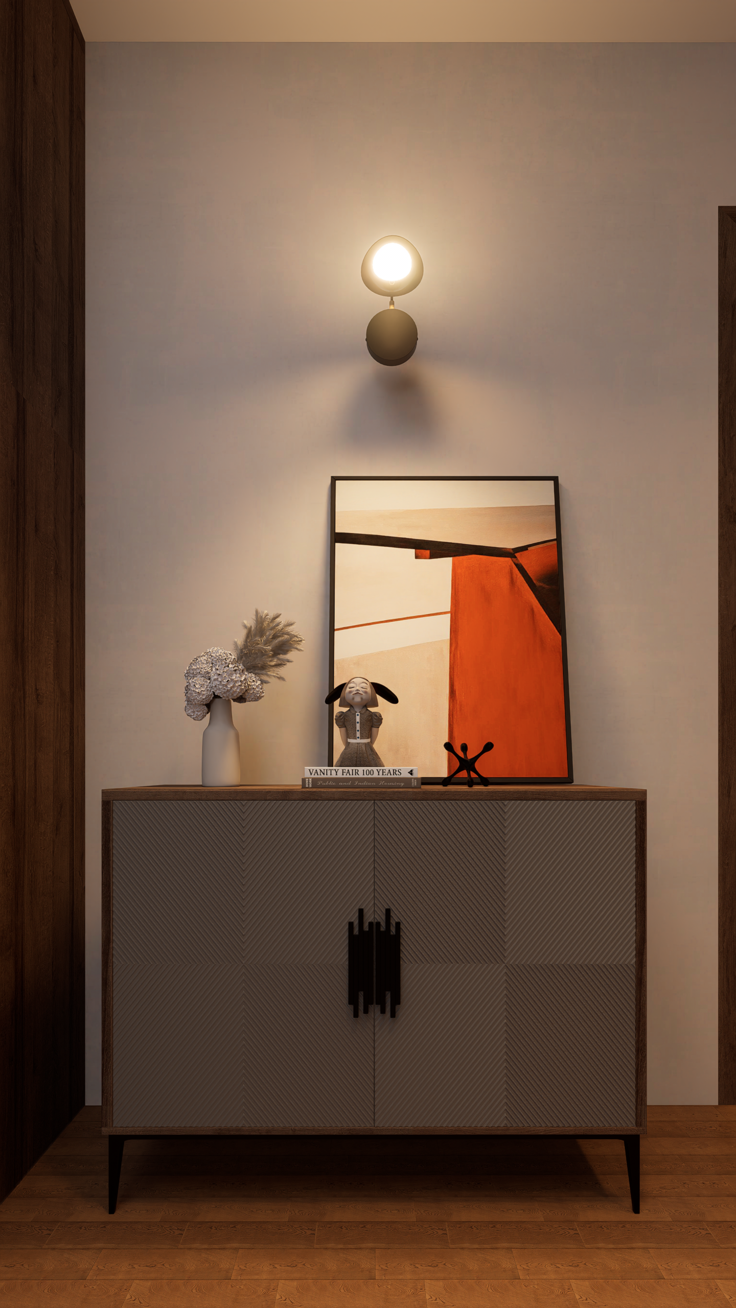 Console with framed abstract art, vase of dried flowers, a small bunny figurine, and books, beneath a warm wall lamp.